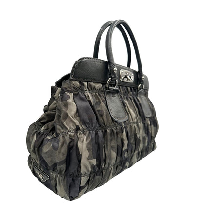 Lato destro di una Borsa Prada in tessuto nylon goffrato trama camouflage nelle tonlità del verde, finiture in pelle nere e inserti metallici argentati; dotata di doppi manici stondati. Completa di dustbag. Originale, usata, di lusso, in ottime condizioni.