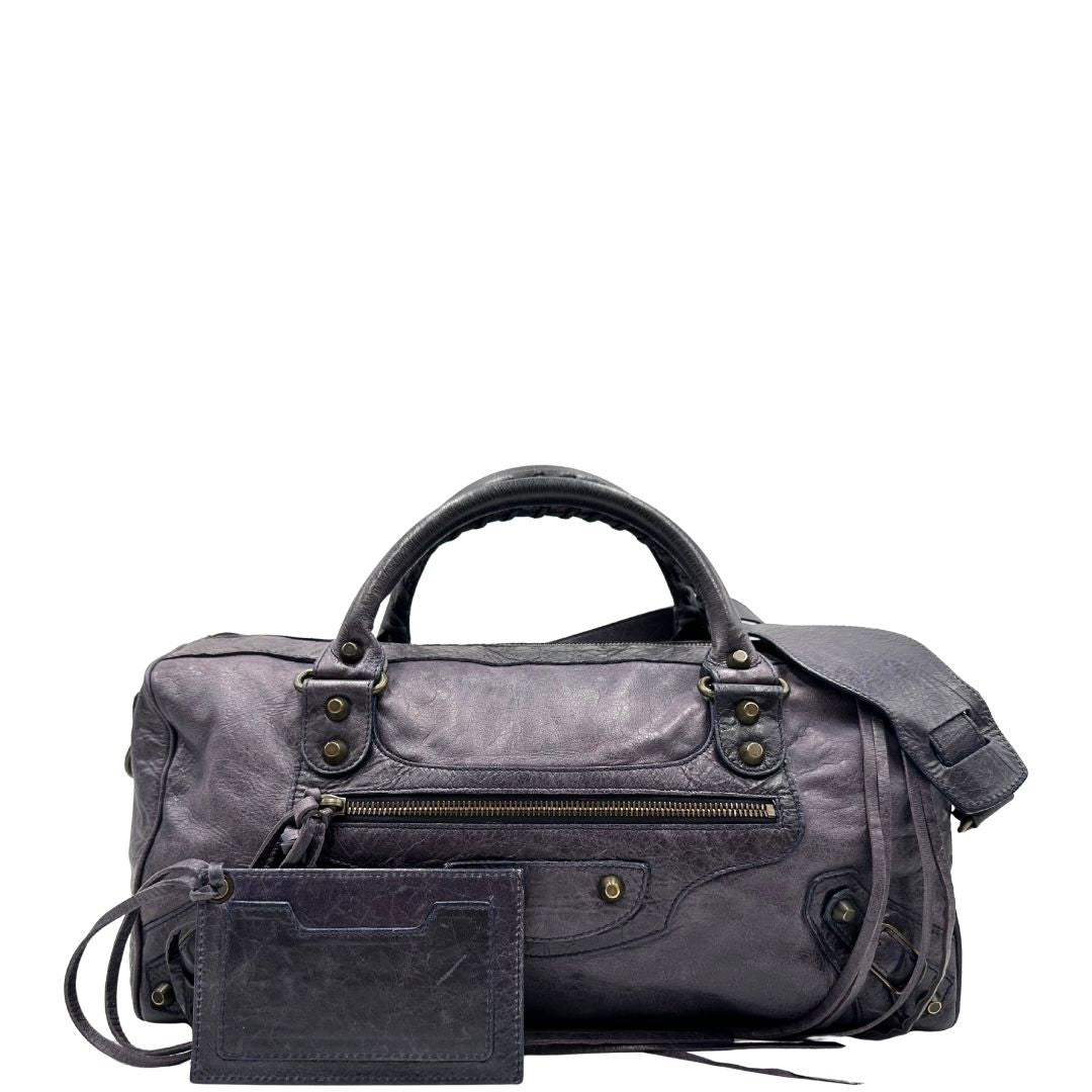 Front di unaBorsa Balenciaga in pelle viola scuro effetto invecchiato con parti metalliche ottone anticato, munita di doppi manici con dettaglio intreccio, e una tracolla amovibile e regolabile con spallaccio. Completa di dustbag. Originale, usata, di lusso, in ottime condizioni.