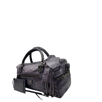 Lato sinistro di una Borsa Balenciaga in pelle viola scuro effetto invecchiato con parti metalliche ottone anticato, munita di doppi manici con dettaglio intreccio, e una tracolla amovibile e regolabile con spallaccio. Completa di dustbag. Originale, usata, di lusso, in ottime condizioni.