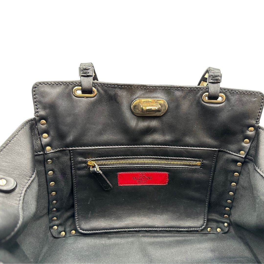 Interno di una Borsa Valentino Garavani in pelle nera con parti metalliche dorate; impreziosita da borchie piramidali e munita di doppi manici e una tracolla amovibile. Completa di dustbag e cartellino. Originale, usata, di lusso, in ottime condizioni.