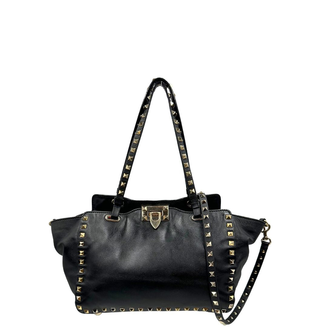 Front di una Borsa Valentino Garavani in pelle nera con parti metalliche dorate; impreziosita da borchie piramidali e munita di doppi manici e una tracolla amovibile. Completa di dustbag e cartellino. Originale, usata, di lusso, in ottime condizioni.