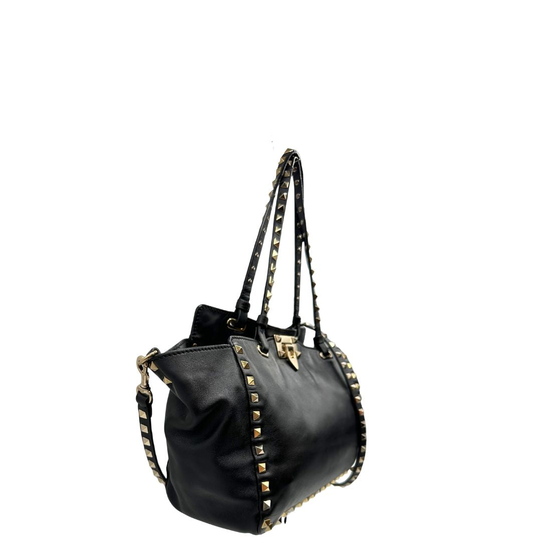 Lato destro di una Borsa Valentino Garavani in pelle nera con parti metalliche dorate; impreziosita da borchie piramidali e munita di doppi manici e una tracolla amovibile. Completa di dustbag e cartellino. Originale, usata, di lusso, in ottime condizioni.