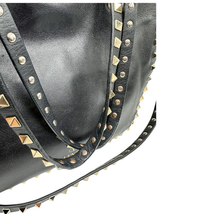 Manici di una Borsa Valentino Garavani in pelle nera con parti metalliche dorate; impreziosita da borchie piramidali e munita di doppi manici e una tracolla amovibile. Completa di dustbag e cartellino. Originale, usata, di lusso, in ottime condizioni.