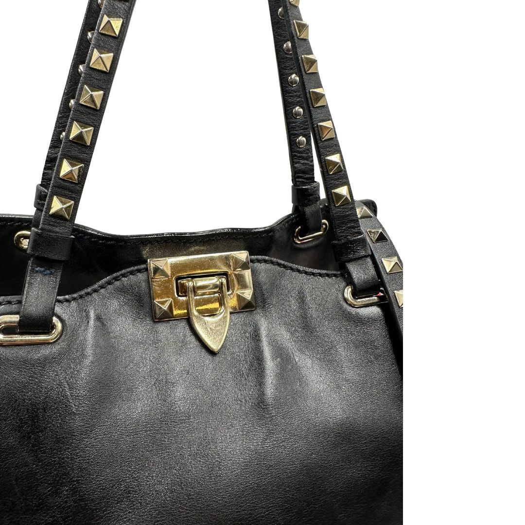 Chiusura di una Borsa Valentino Garavani in pelle nera con parti metalliche dorate; impreziosita da borchie piramidali e munita di doppi manici e una tracolla amovibile. Completa di dustbag e cartellino. Originale, usata, di lusso, in ottime condizioni.