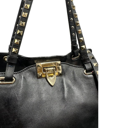 Chiusura di una Borsa Valentino Garavani in pelle nera con parti metalliche dorate; impreziosita da borchie piramidali e munita di doppi manici e una tracolla amovibile. Completa di dustbag e cartellino. Originale, usata, di lusso, in ottime condizioni.