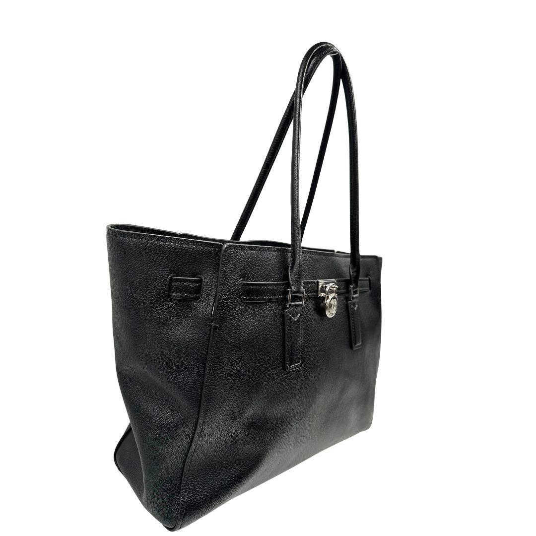 Laterale sinistro di una borsa Michael Kors in pelle nera con parti metalliche argentate; munita di doppi manici. Completa di dustbag. Indossabile a spalla.