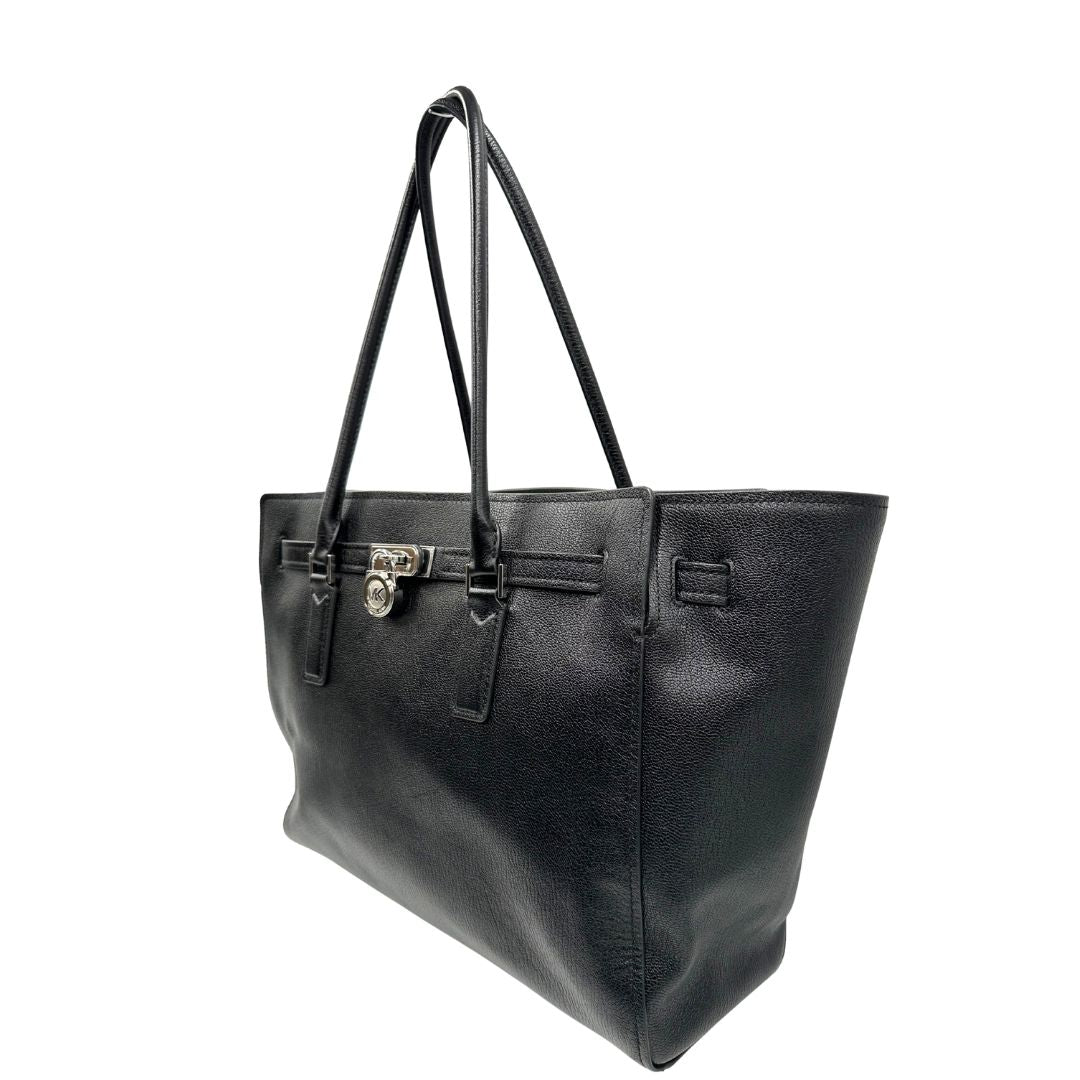 Laterale destro di una borsa Michael Kors in pelle nera con parti metalliche argentate; munita di doppi manici. Completa di dustbag. Indossabile a spalla.