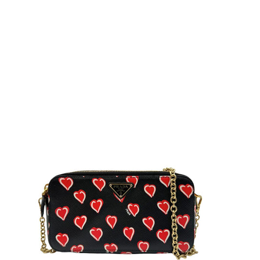 Front, Prada WOC in pelle saffiano nera decorata con una vivace stampa a cuori rossi. indossabile a tracolla oppure a mano. Originale, usata, di lusso, in ottime condizioni.