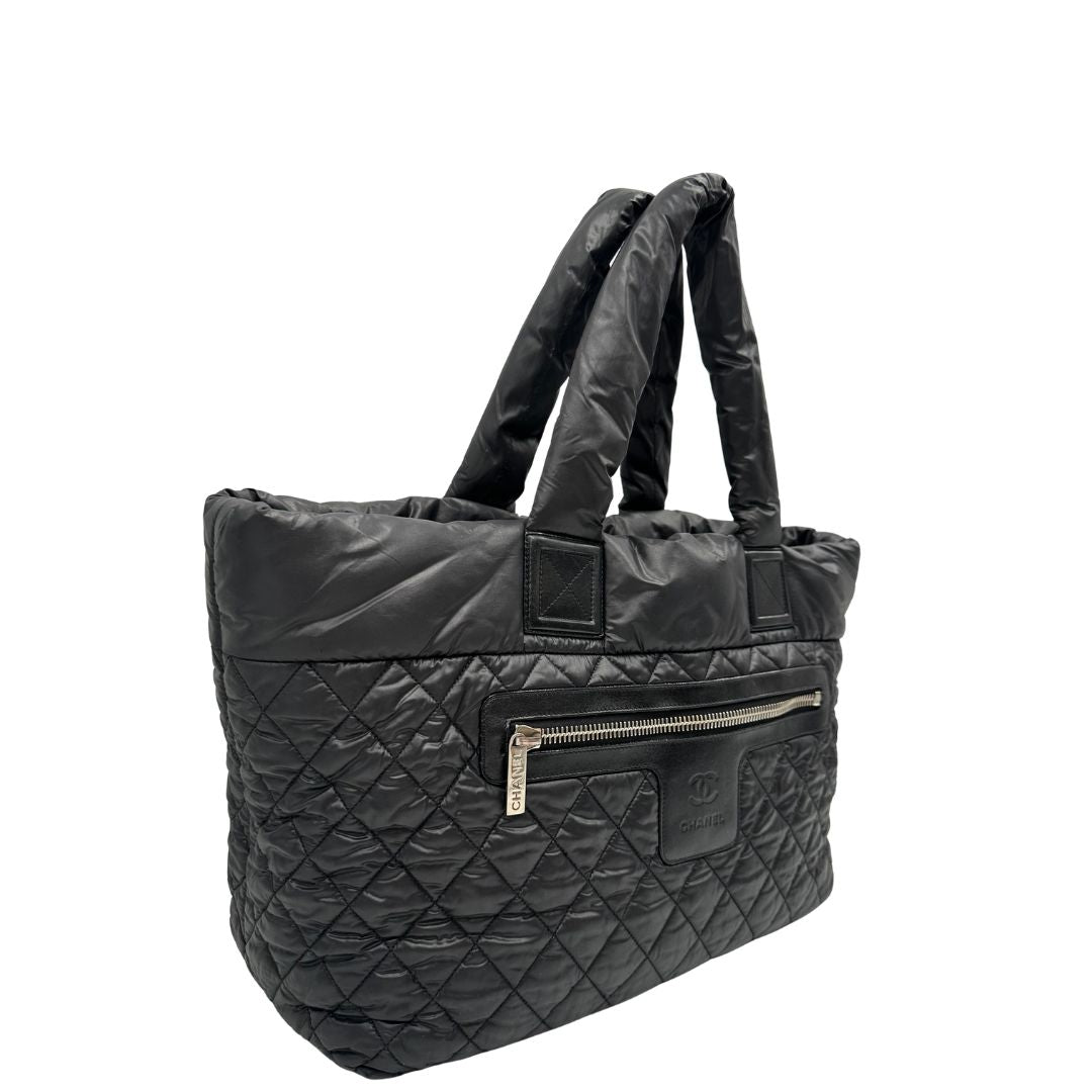lato Chanel in nylon trapuntato nero, caratterizzata da design morbido e leggero con iconico motivo matelassé. Dotata di doppi manici imbottiti, tasca frontale con zip e dettagli argentati, di lusso, originale, ottime condizioni. 