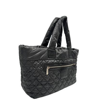 lato Chanel in nylon trapuntato nero, caratterizzata da design morbido e leggero con iconico motivo matelassé. Dotata di doppi manici imbottiti, tasca frontale con zip e dettagli argentati, di lusso, originale, ottime condizioni. 