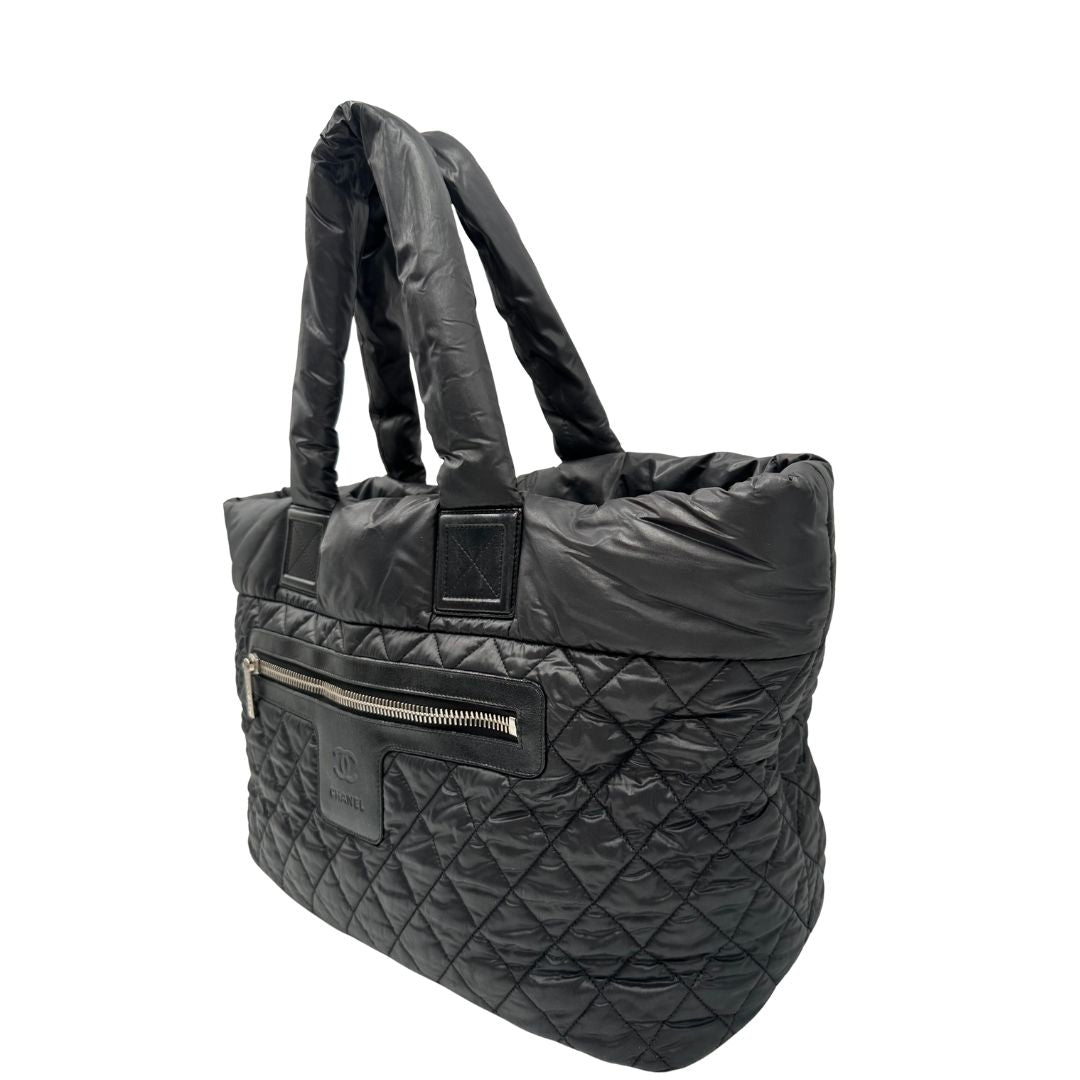 lato Chanel in nylon trapuntato nero, caratterizzata da design morbido e leggero con iconico motivo matelassé. Dotata di doppi manici imbottiti, tasca frontale con zip e dettagli argentati, di lusso, originale, ottime condizioni. 