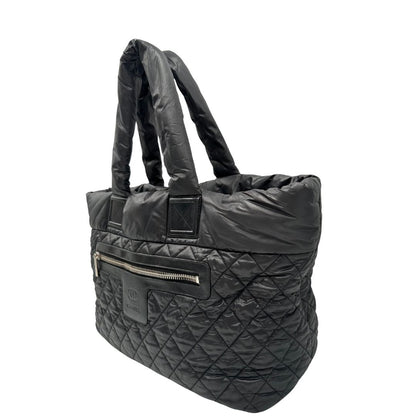 lato Chanel in nylon trapuntato nero, caratterizzata da design morbido e leggero con iconico motivo matelassé. Dotata di doppi manici imbottiti, tasca frontale con zip e dettagli argentati, di lusso, originale, ottime condizioni. 