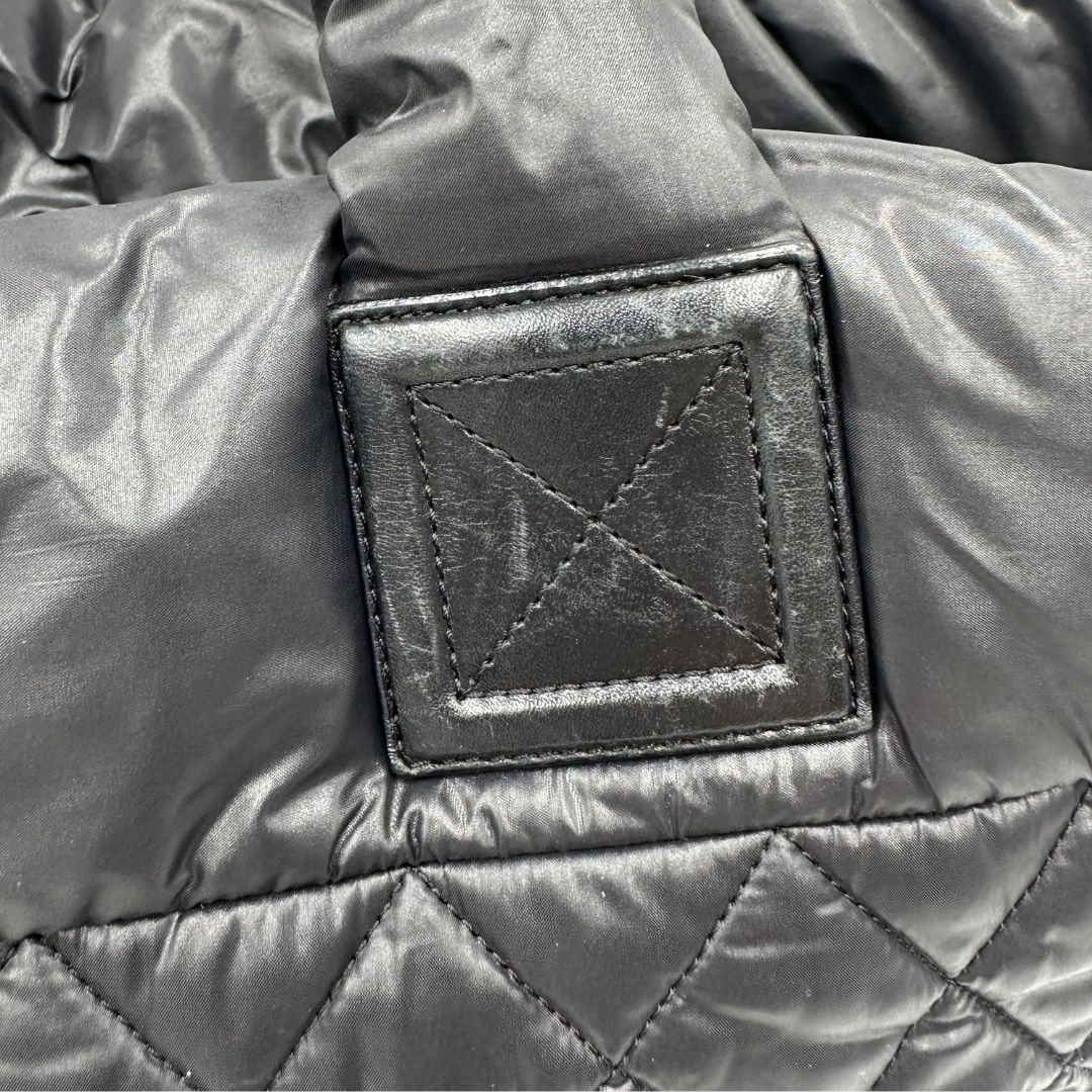 Chanel in nylon trapuntato nero, caratterizzata da design morbido e leggero con iconico motivo matelassé. Dotata di doppi manici imbottiti, tasca frontale con zip e dettagli argentati, di lusso, originale, ottime condizioni.