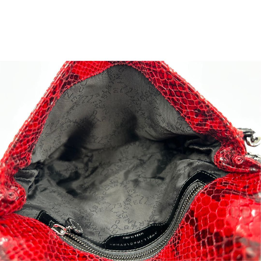 Interno, Borsa Stella McCartney, modello compatto e grintoso, realizzata in ecopelle effetto pitone rosso lucido e impreziosita da dettagli con catena metallica nera lungo i bordi. Indossabile a tracolla. Originale, usata, di lusso, in ottime condizioni.