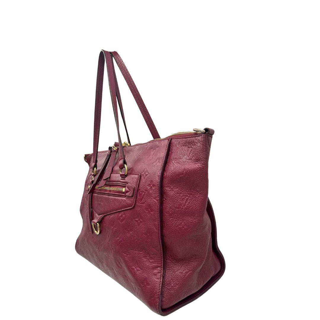 Laterale, Louis Vuitton in pelle monogram empreinte color magenta con hardware dorato , munita di doppi manici. Indossabile a spalla. Originale, usata, di lusso, in ottime condizioni.