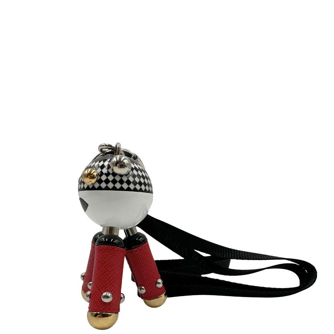 Charm Prada presenta una testa a sfera con un motivo a scacchi bianchi e neri e dettagli metallici color oro, le gambe sono realizzate in pelle saffiano rossa. Originale, usato, di lusso, in condizioni eccellenti.