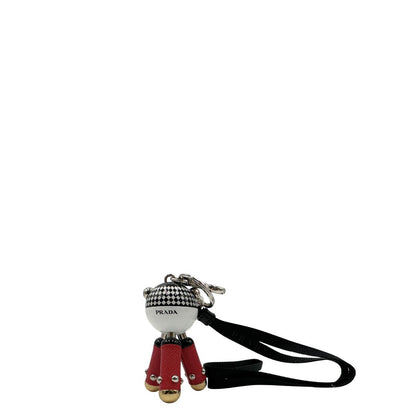 Charm Prada presenta una testa a sfera con un motivo a scacchi bianchi e neri e dettagli metallici color oro, le gambe sono realizzate in pelle saffiano rossa. Originale, usato, di lusso, in condizioni eccellenti.