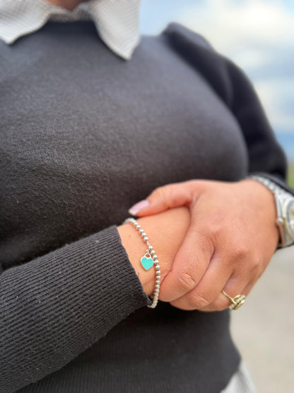 Ragazza che mostra un bracciale Tiffany&Co. della collezione Return to Tiffany in argento 925 composto da sfere circolari e ciondolo cuore smaltato in verde Tiffany. Completo di scatola e sacchetto anti polvere.