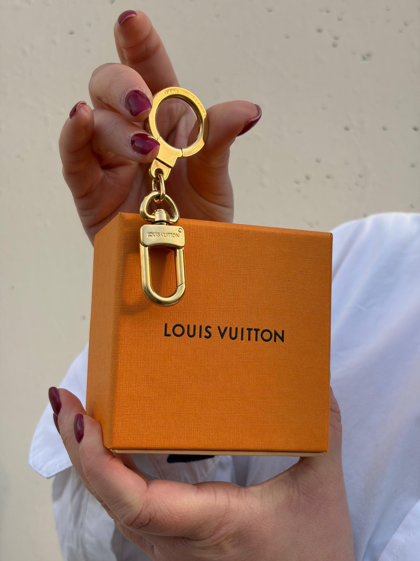 Ragazza che mostra un charm portachiavi LV in metallo dorato, corredato, usato, originale, second hand, in ottime condizioni.