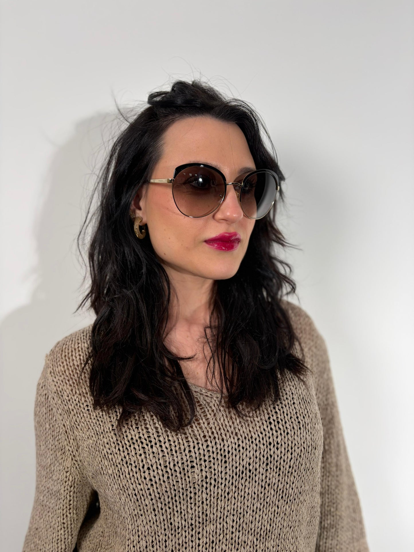 Ragazza che indossa un paio di occhiali da sole Prada caratterizzati da una montatura nera lucida con lenti sfumate grigie, asticelle maculate e hardware dorato, usati, originali, second hand, in ottime condizioni.